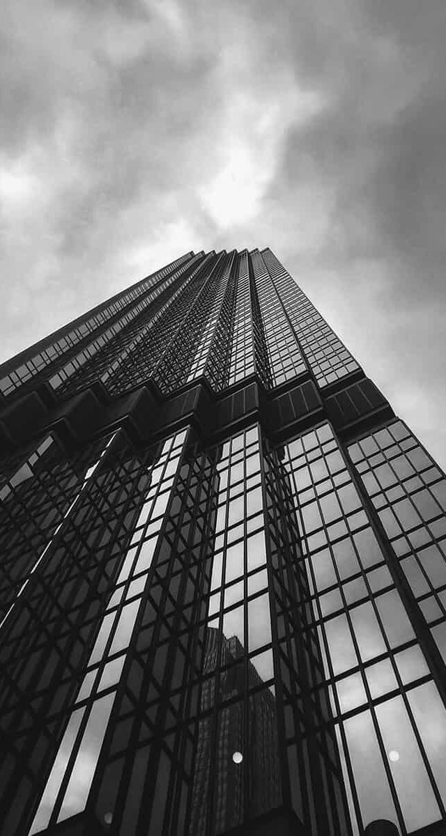A black and white picture form the bottom of a skyscraper looking up in the sky